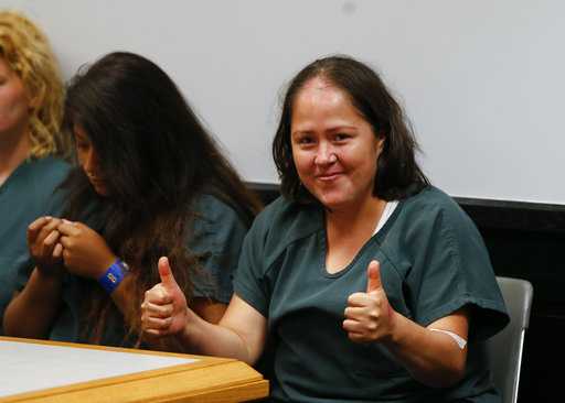 Woman charged in slayings of 4 children, dad smiles in court